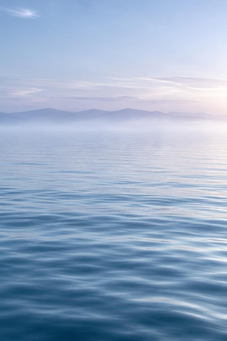 Calm water and misty mountains at dawn